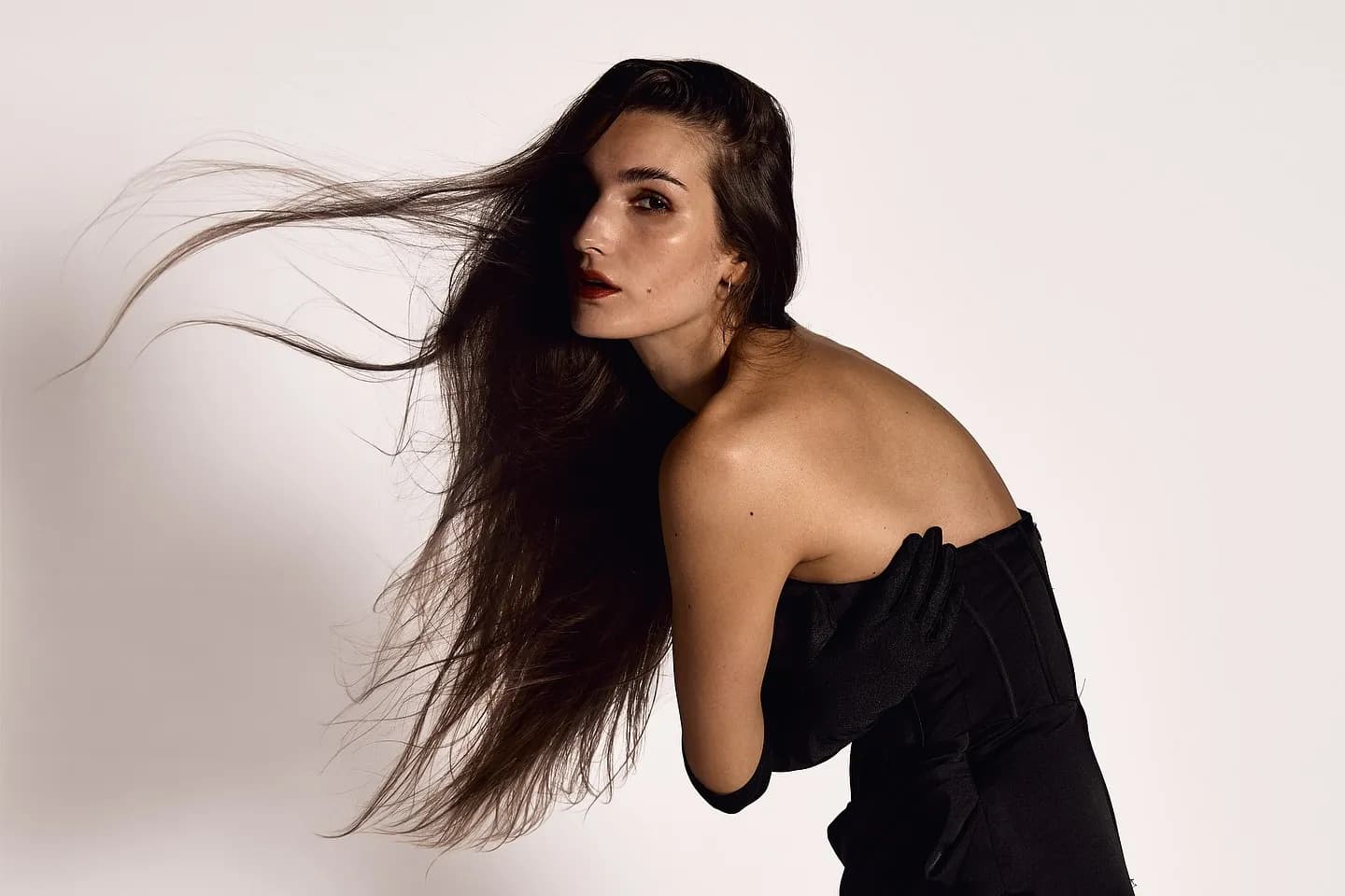Fashion photography — a model in a black gown, hair caught mid-motion in studio light