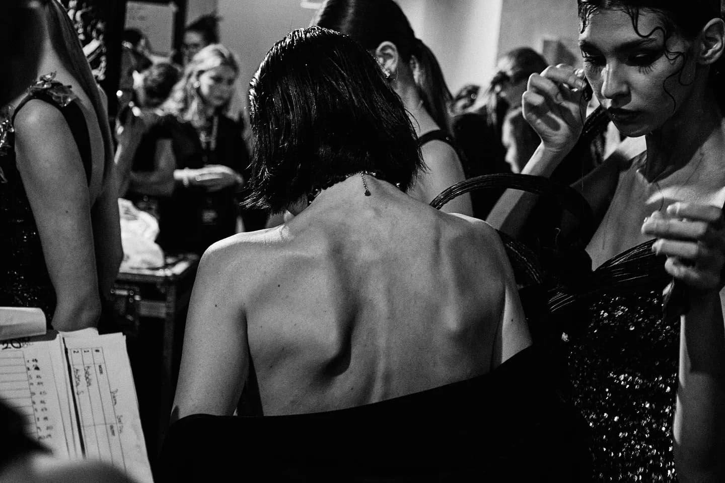 Backstage before a fashion show — models in couture being prepared under work light